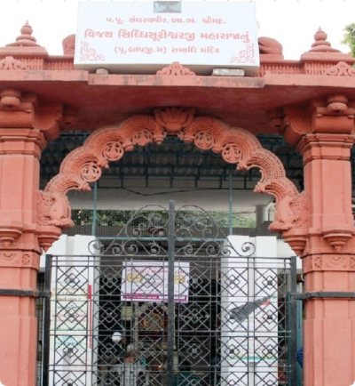 Jain temple entrance with red arched gateway and carvings in Ahmedabad, India.